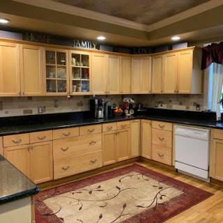 A modern kitchen featuring wooden cabinets, black countertops, and a decorative rug.