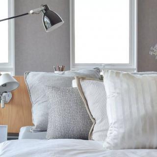 A cozy bedroom with neatly arranged pillows and a modern reading lamp.