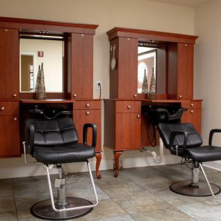 A stylish hair salon interior featuring two black salon chairs with wooden cabinets and mirrors.