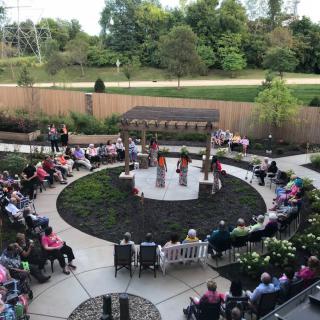 A group of people gathered in a circular outdoor garden setting for a ceremony or event.