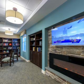 A cozy library corner with bookshelves, a television above a fireplace, and soft lighting.
