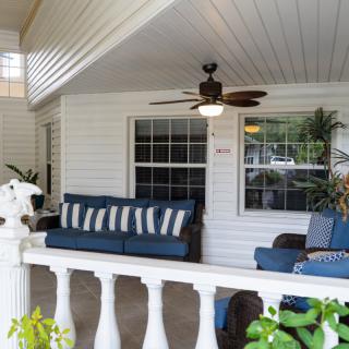 A cozy porch with comfortable seating and a ceiling fan surrounded by greenery.
