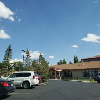 A view of a building surrounded by trees and parked vehicles under a clear blue sky.