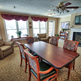A cozy living room featuring a dining table with chairs, comfortable sofas, a fireplace, and large windows.