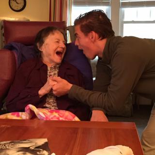 A joyful interaction between an elderly woman and a caregiver, both laughing and enjoying the moment indoors.
