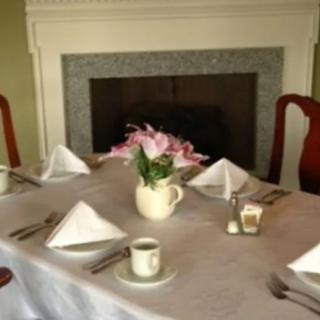 A neatly arranged dining table with folded napkins, tea cups, and a flower centerpiece in front of a fireplace.