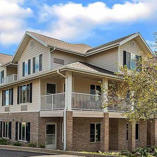 A residential building with a porch and multiple windows under a partly cloudy sky.