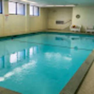 An indoor swimming pool with clear blue water, surrounded by beige walls and windows.