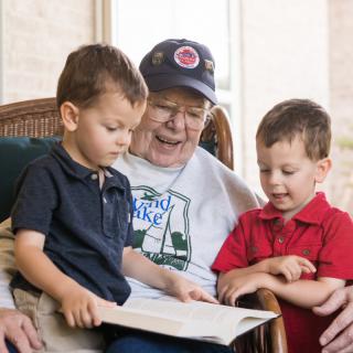 An elderly man reads a book with two young boys.