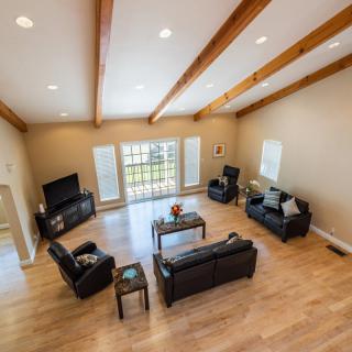 A spacious living room featuring modern leather furniture, wooden beams, and ample natural light streaming through large windows.