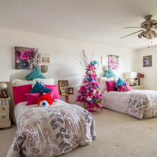 A vibrant bedroom with twin beds featuring colorful pillows and a festive Christmas tree in the corner.