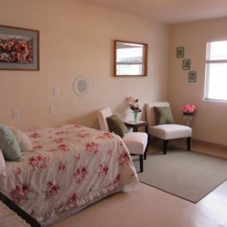 A cozy bedroom with a bed adorned with floral bedding, two chairs, and decorative elements like paintings and wall art.