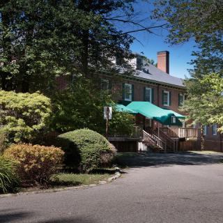A brick house surrounded by lush greenery and trees, featuring a green canopy over the entrance.