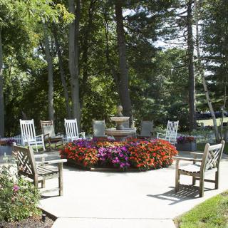 A well-arranged outdoor patio area with wooden chairs surrounding a central flower display, set amidst lush trees.