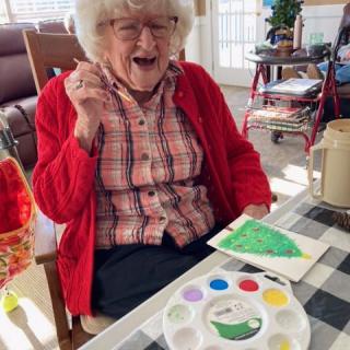 An elderly woman joyfully working on a painting project with art supplies.