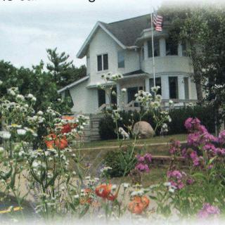 A charming house surrounded by a vibrant flower garden with an American flag flying in the yard.