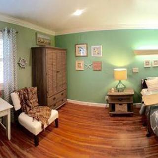 A cozy and well-decorated bedroom featuring green walls, wooden flooring, and a blend of furniture including a bed, wardrobe, lamp, and chair.