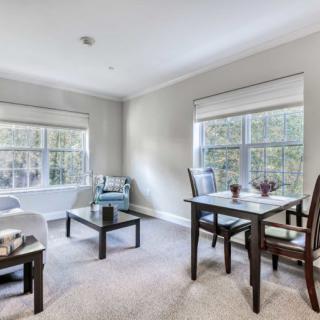 A modern living room with ample natural light, featuring cozy seating and a dining area.