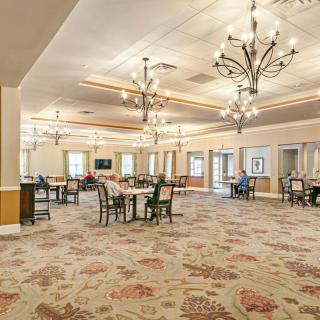 A spacious and elegantly decorated dining area featuring chandeliers and well-arranged tables and chairs.