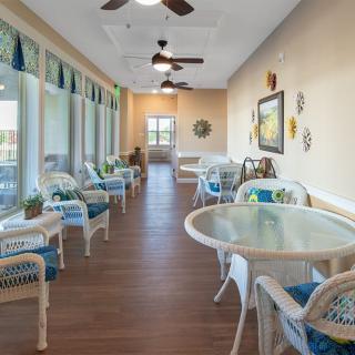 A cozy indoor seating area with tables and chairs, featuring large windows and ceiling fans.