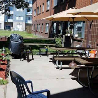 A cozy outdoor patio area with seating and umbrellas, surrounded by greenery and apartment buildings.