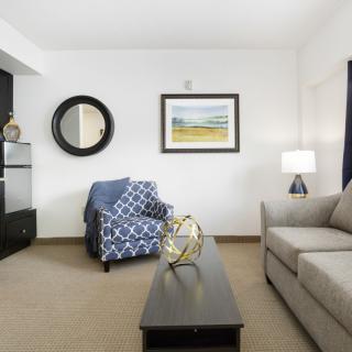 A modern living room with a comfortable sofa and armchair, complemented by stylish decor, including a round mirror and landscape artwork.