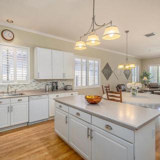 A modern kitchen with white cabinets and a central island, featuring wooden floors and pendant lighting.