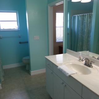 A clean and bright bathroom with turquoise walls, featuring a sink, mirror, toilet, and shower.
