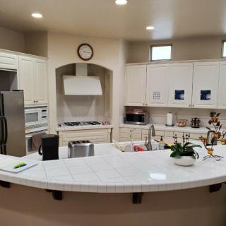 A modern kitchen with white cabinetry and a spacious countertop, featuring various appliances and decorative plants.