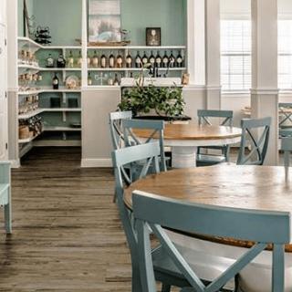 A cozy cafe interior with wooden tables and chairs, featuring shelves stocked with various items.