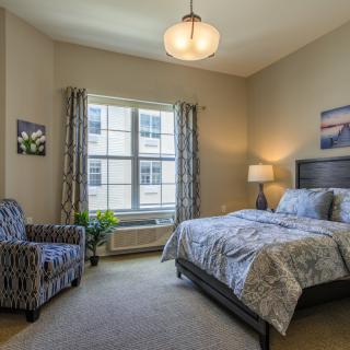 A cozy bedroom with a bed, armchair, and large window allowing natural light.