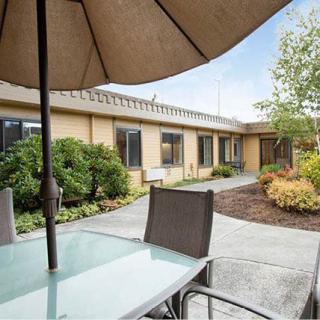 A tranquil outdoor patio area with a table, chairs, and an umbrella, surrounded by garden landscaping.