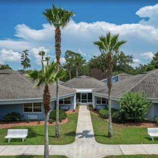 A building surrounded by palm trees with a neatly landscaped garden and pathway leading to the entrance.
