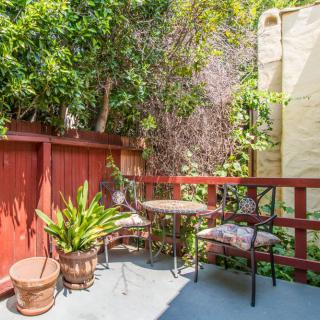 A small, sunny patio with a table and two chairs surrounded by lush plants.