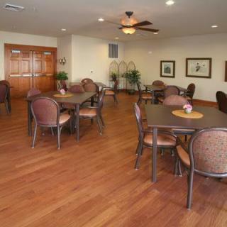 A spacious dining area with several tables and chairs, featuring wooden floors and a ceiling fan.