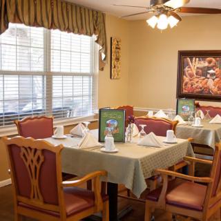 A well-decorated dining area with neatly arranged tables and chairs, featuring elegant table settings and wall art.