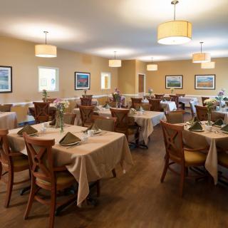 A spacious dining room with elegantly set tables and comfortable chairs, featuring warm lighting and tasteful decor.
