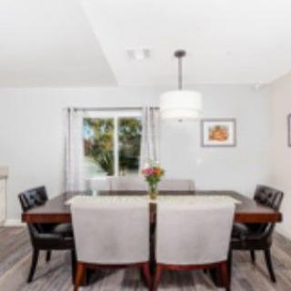 A modern dining room with a large table, surrounded by chairs and illuminated by a stylish light fixture.