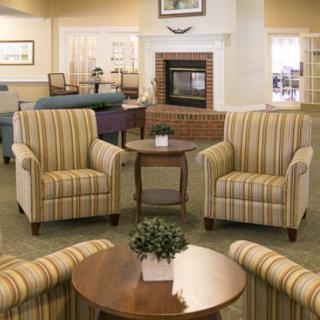 A cozy living room seating area with striped armchairs and coffee tables in front of a fireplace.