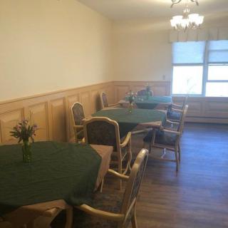 A cozy dining room with tables covered in green tablecloths, surrounded by chairs and illuminated by a chandelier.