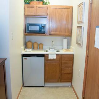 A compact kitchenette featuring a microwave, sink, mini fridge, and wooden cabinets.