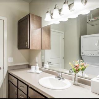 A modern bathroom featuring a sleek vanity, mirror, and an in-unit laundry setup.
