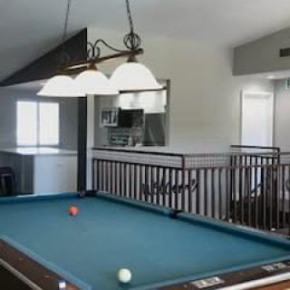 A spacious recreational room featuring a pool table under stylish lighting.