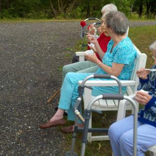 A group of seniors sitting in chairs outdoors, enjoying a leisurely moment with their walkers nearby.