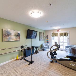 A modern exercise room equipped with a treadmill, stationary bike, and television, featuring wooden floors and large windows.