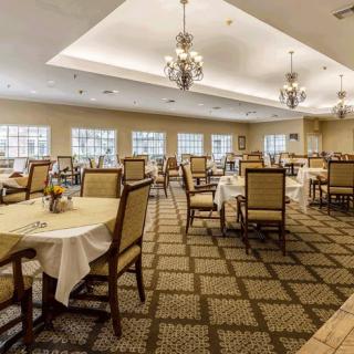 An elegant dining room with neatly arranged tables and chairs, featuring chandeliers and large windows.