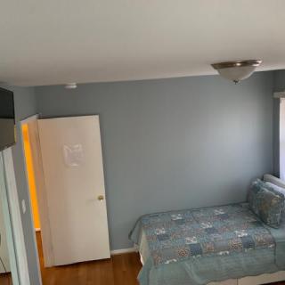 A minimalist bedroom featuring blue walls, a bed with patterned covers, and a small window.