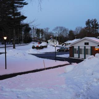 A serene winter evening scene with a blanket of snow covering the ground and soft lighting from a lamp post.