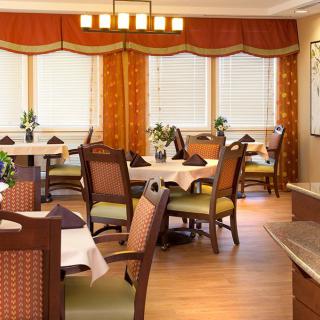 A cozy dining area with elegantly arranged tables and chairs, featuring large windows adorned with orange curtains.