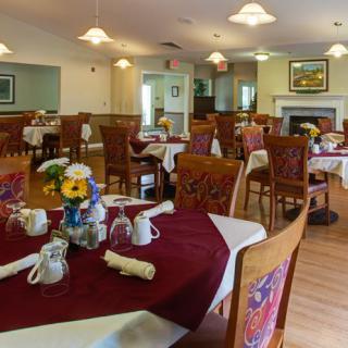 A cozy dining room with tables set for a meal, featuring warm lighting and floral decorations.